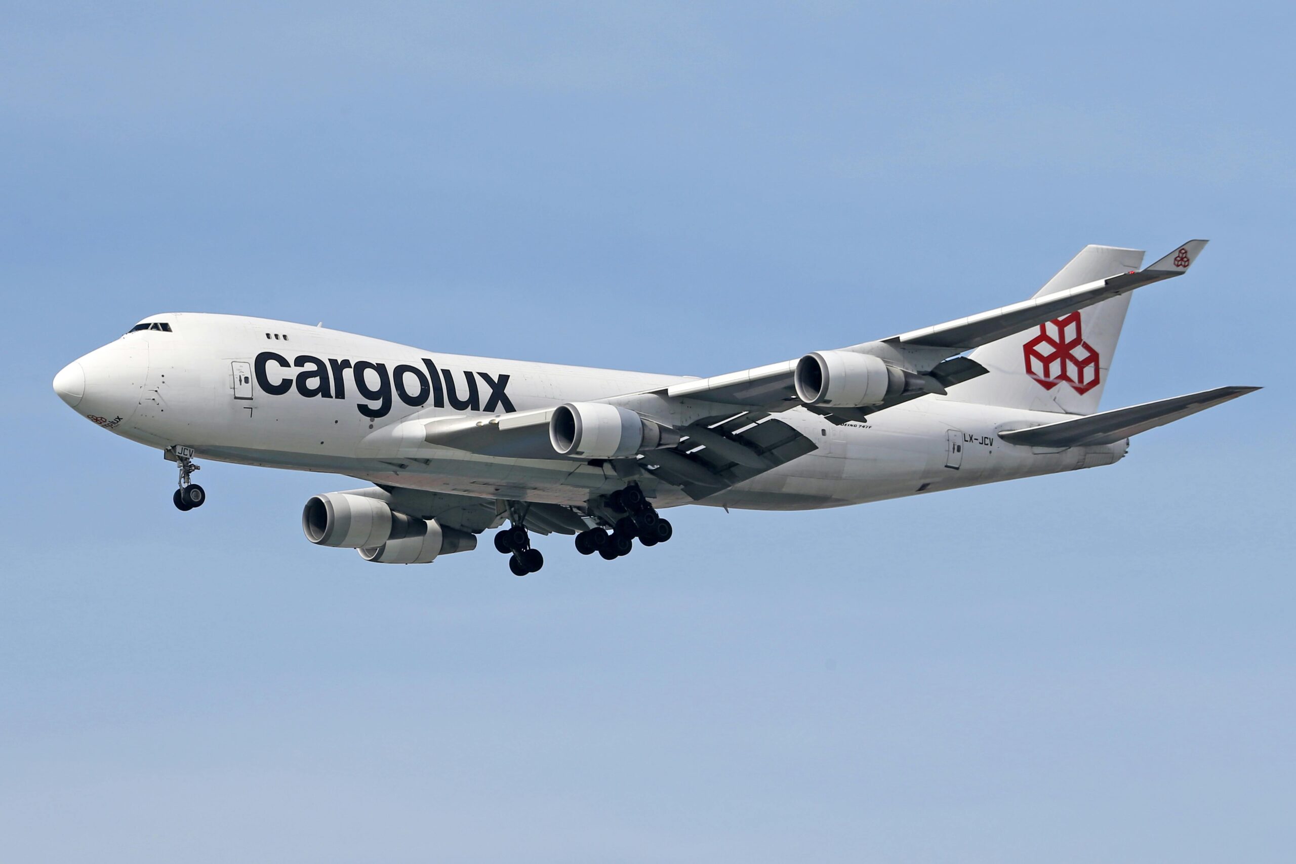 A Cargolux cargo aircraft flying with wheels down under a clear blue sky.
